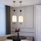 Close-up of two Clérachic white pendants lit in a grey panelled room, with a black marble table and a pale banquette below.