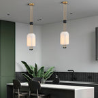 Two Clérachic pendants at different heights in an open kitchen with a deep green wall, a black counter and a large leafy plant.