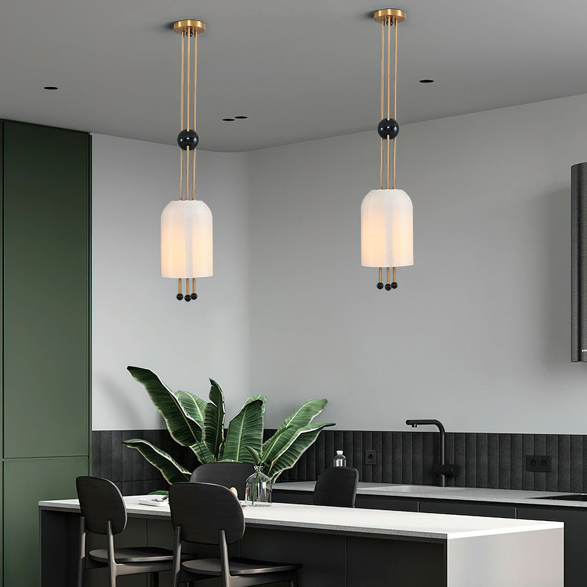 Two Clérachic pendants at different heights in an open kitchen with a deep green wall, a black counter and a large leafy plant.
