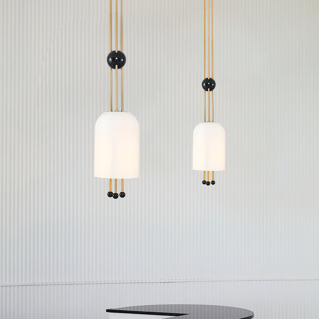 Two Clérachic white pendants of different sizes against a pale fluted wall, each on three brass rods with a black ball.