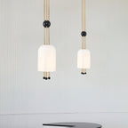Two Clérachic white pendants of different sizes against a pale fluted wall, each on three brass rods with a black ball.