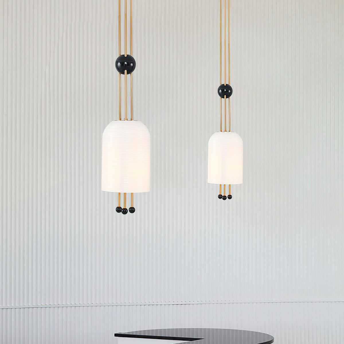 Two Clérachic white pendants of different sizes against a pale fluted wall, each on three brass rods with a black ball.