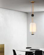 A Clérachic white pendant hung against a grey plaster wall, with a round white table and black chairs below.