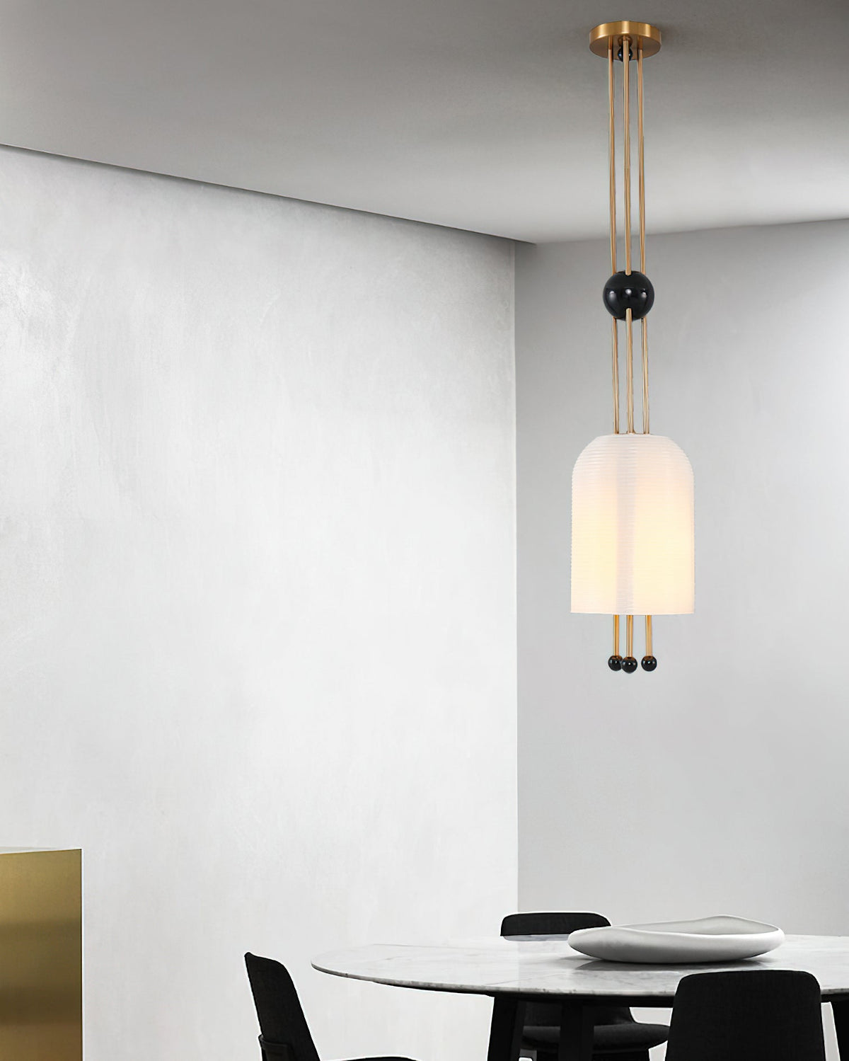 A Clérachic white pendant hung against a grey plaster wall, with a round white table and black chairs below.