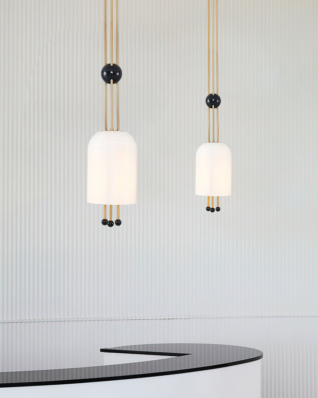 Two Clérachic pendants, one larger and one smaller, hanging against a fluted pale wall above a curved black counter.