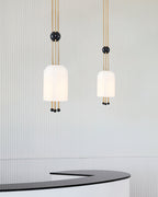 Two Clérachic pendants, one larger and one smaller, hanging against a fluted pale wall above a curved black counter.