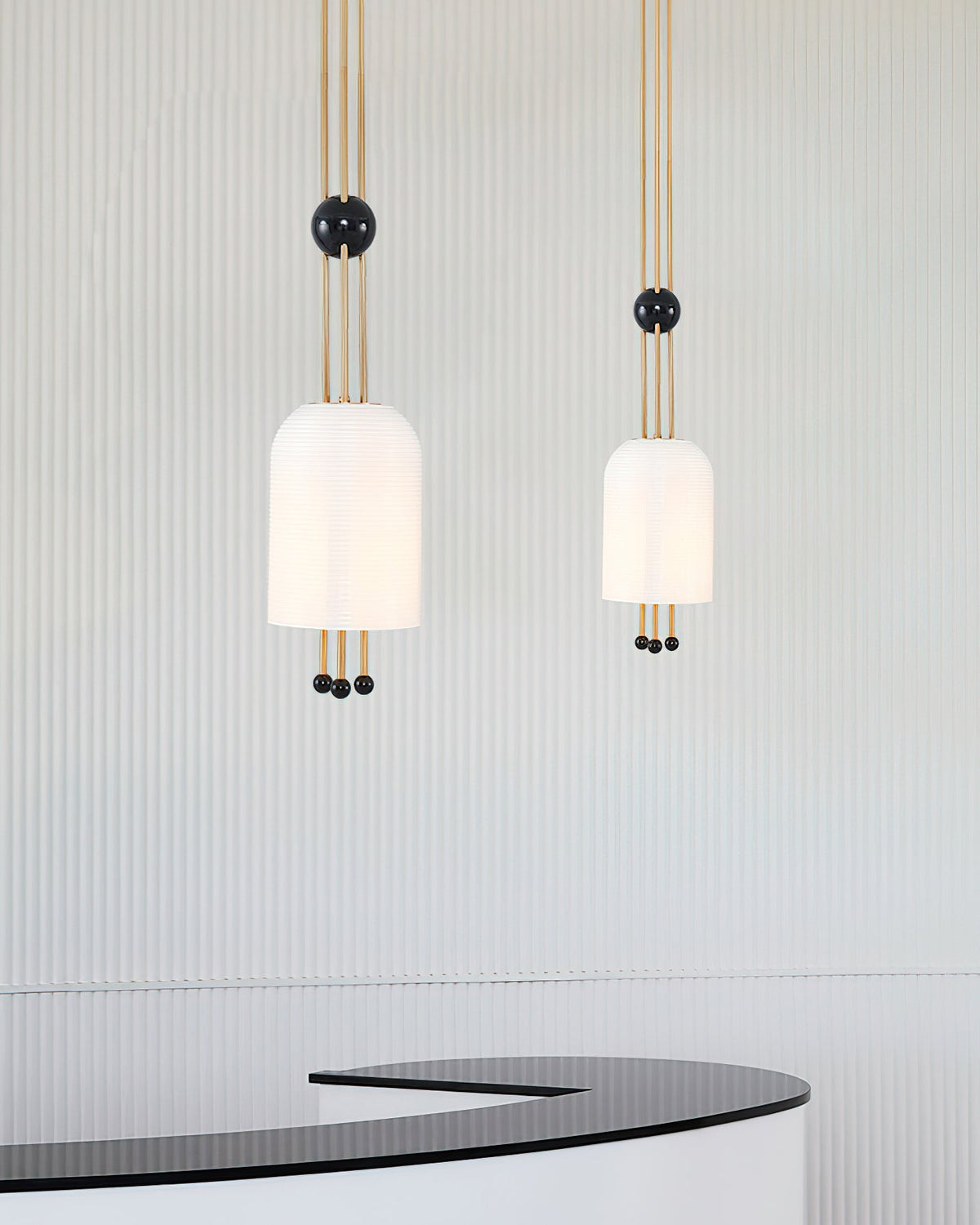 Two Clérachic pendants, one larger and one smaller, hanging against a fluted pale wall above a curved black counter.