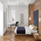A Clérachic pendant hung low by a bed with a navy upholstered headboard, in a bright room with a herringbone floor and a desk.