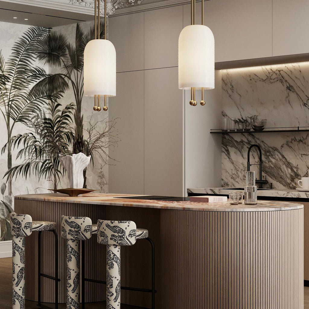 Two Clérachic pendants over a curved, fluted kitchen island with patterned stools, in front of a marble splashback and a palm mural.