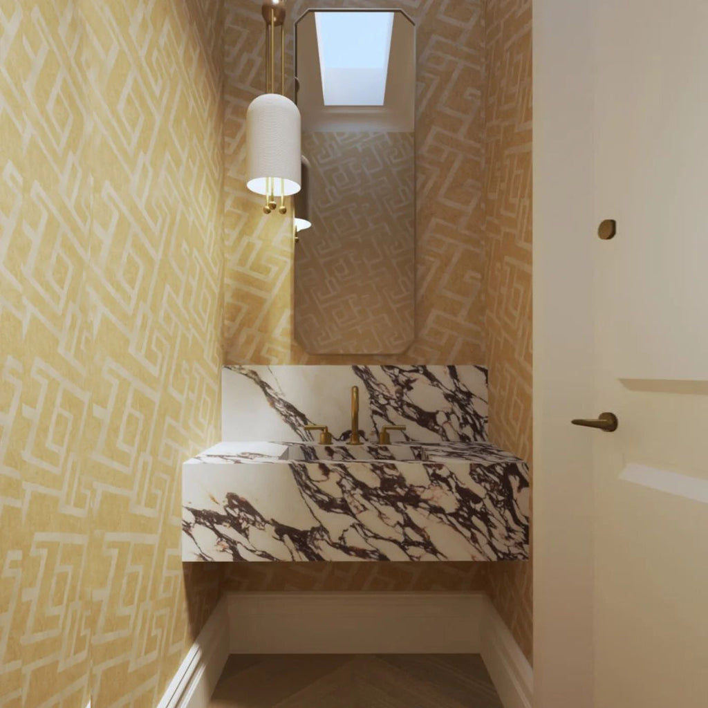 A Clérachic pendant hanging beside a mirror above a marble basin, in a small washroom with gold patterned wallpaper.