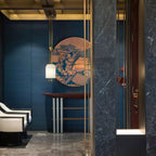 A Clérachic pendant in front of a round blue-and-copper artwork on a deep blue wall, above a red-topped console table.