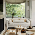 This Clérachic pendant on a pale wall by a large window onto trees, with a boucle sofa and low round tables below.