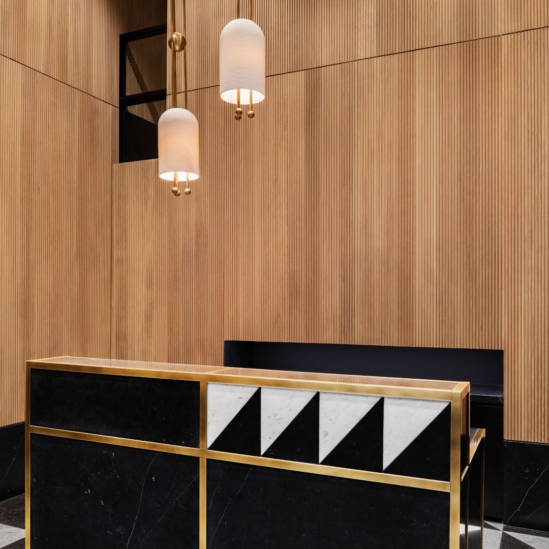 Two Clérachic pendants hung at different heights against a ribbed oak wall, above a brass-framed black and white console.