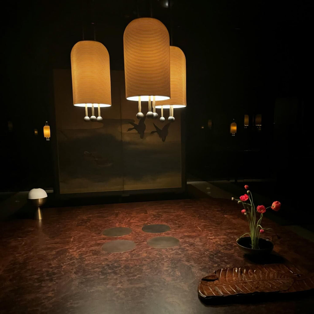 Three Clérachic pendants glowing amber in a dark room, their ribbed shades at different heights over a copper-toned floor.