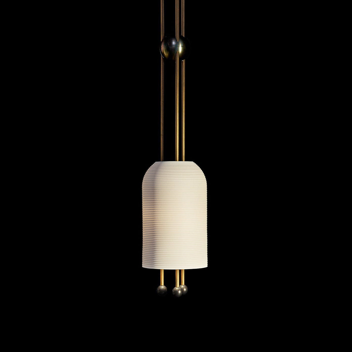 A single Clérachic ribbed white pendant on a black backdrop, lit from within, with two brass rods and balls below the shade.