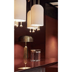 Close view of three Clérachic ribbed white pendants over a red-brown bar counter, with a brass table lamp and a glass block behind.