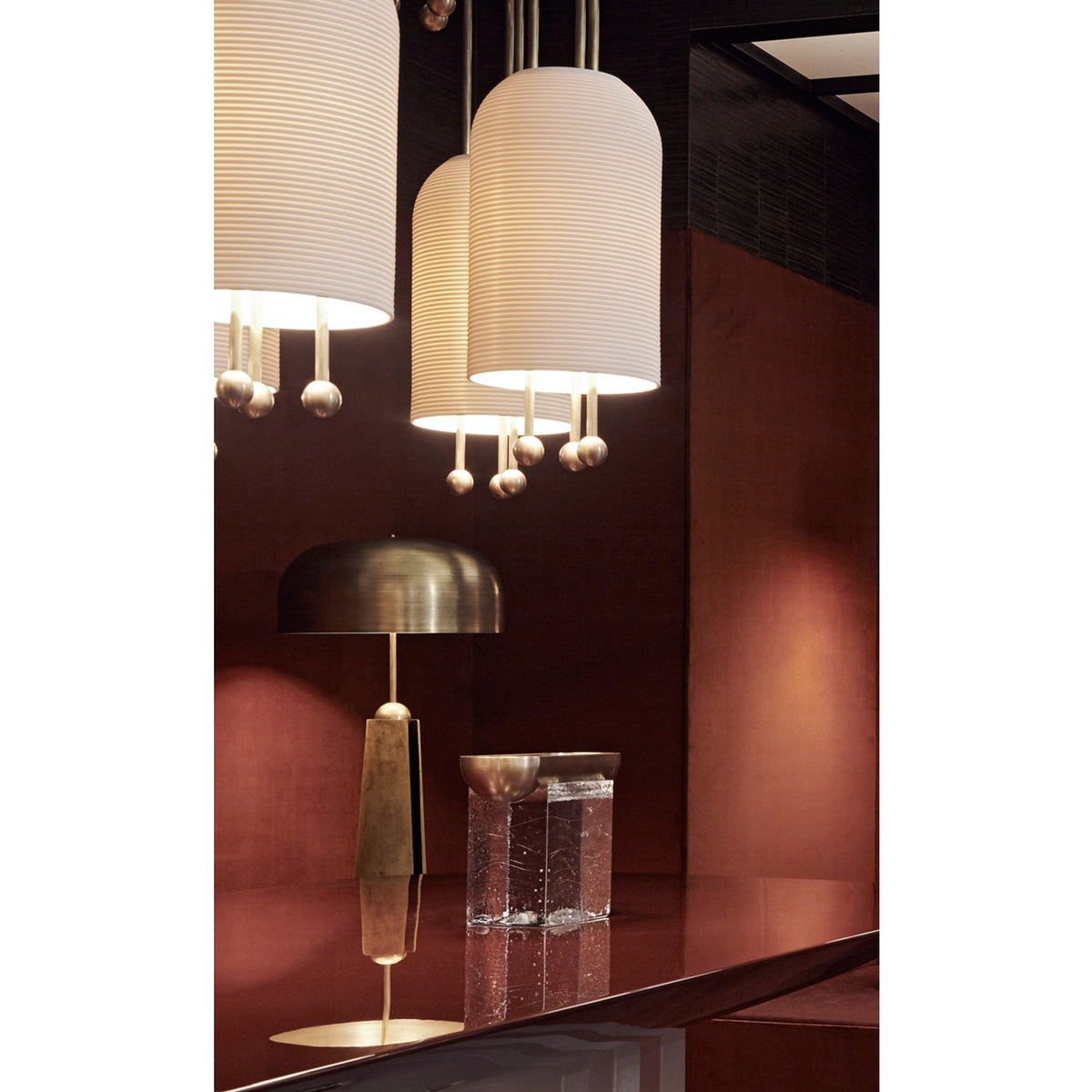 Close view of three Clérachic ribbed white pendants over a red-brown bar counter, with a brass table lamp and a glass block behind.