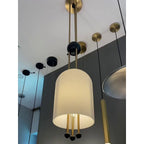 Looking up at this Clérachic pendant, its ribbed white shade lit and three brass-and-black balls below, in a showroom with other lights.