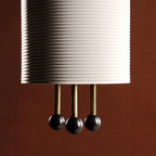 Close view of the horizontal ribbing on the shade of this Clérachic pendant and the three brass rods ending in black balls.