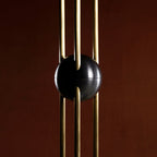 Close view of the black ball clamped around three brass rods on this Clérachic pendant, against a dark red-brown backdrop.