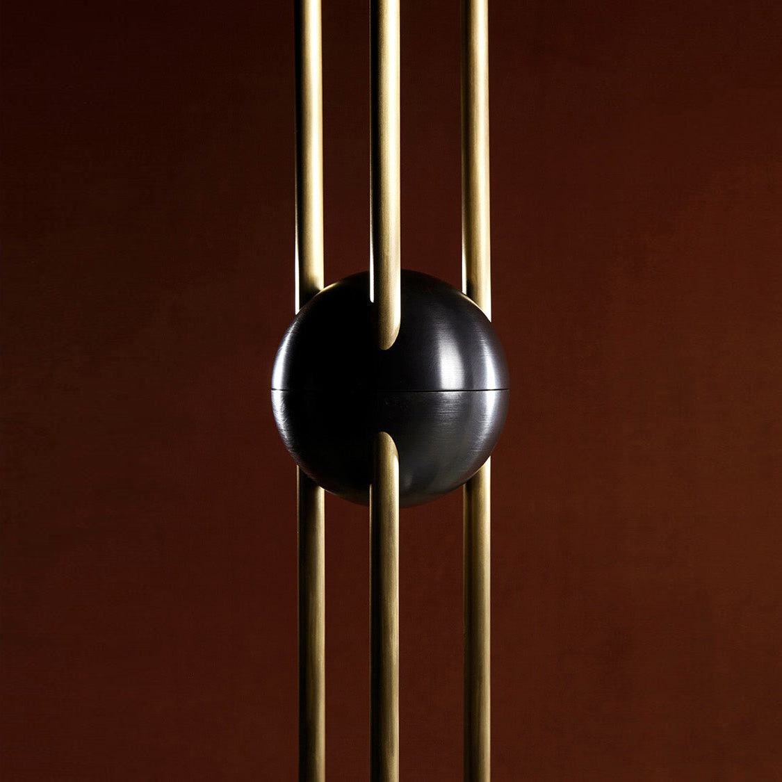 Close view of the black ball clamped around three brass rods on this Clérachic pendant, against a dark red-brown backdrop.