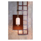 A Clérachic pendant lit against a wooden panel and a red-framed lattice on a rough concrete wall.