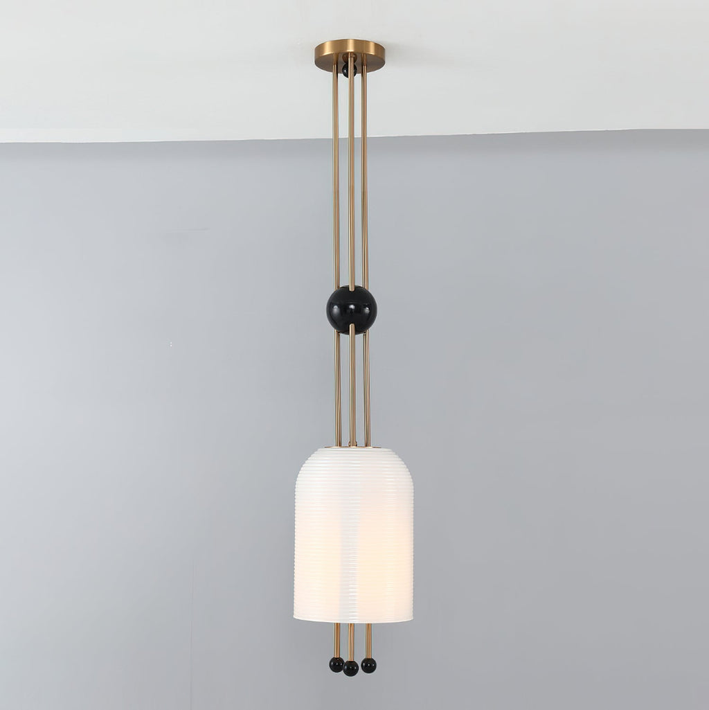 A Clérachic pendant lit against a grey wall, the ribbed white shade hung below a black ball on three brass rods.