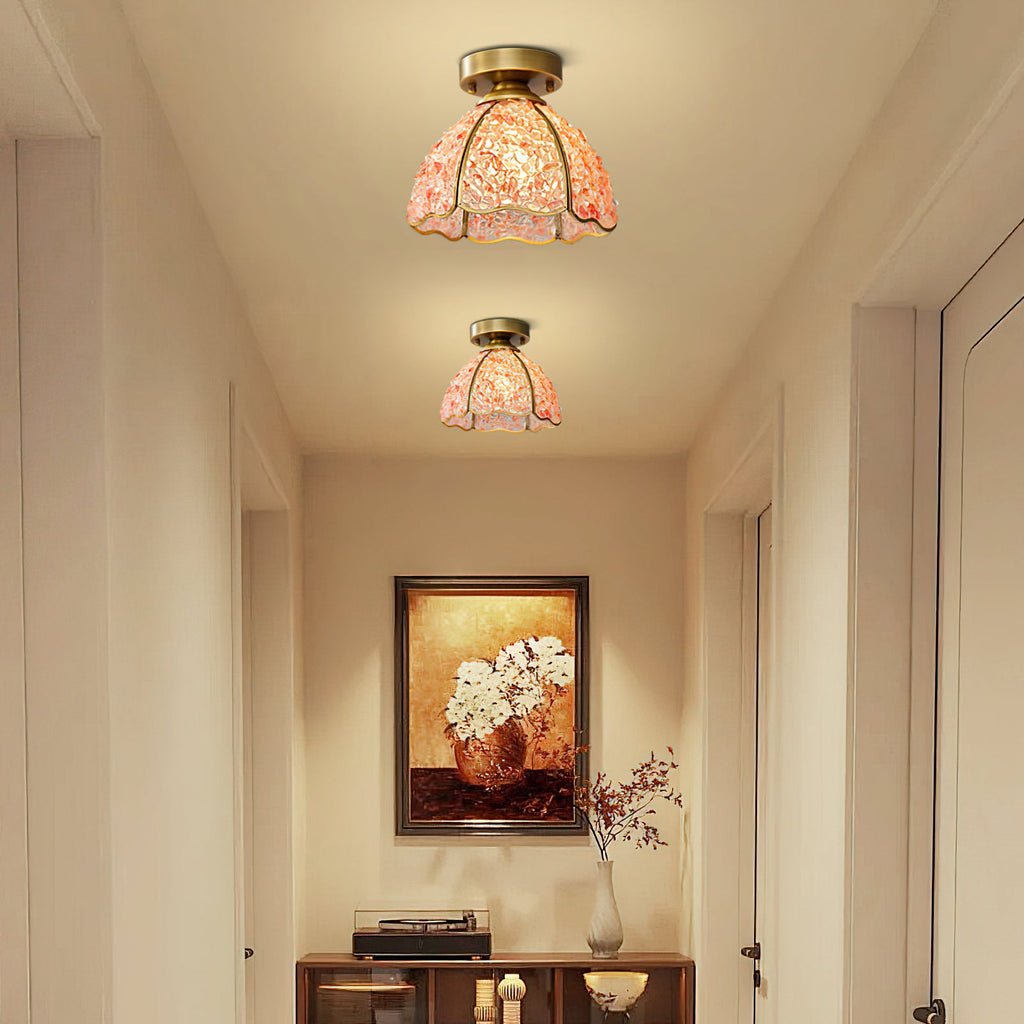 Two pink Clérachic flush ceiling lights glowing in a cream hallway, with a framed floral painting at the far end.