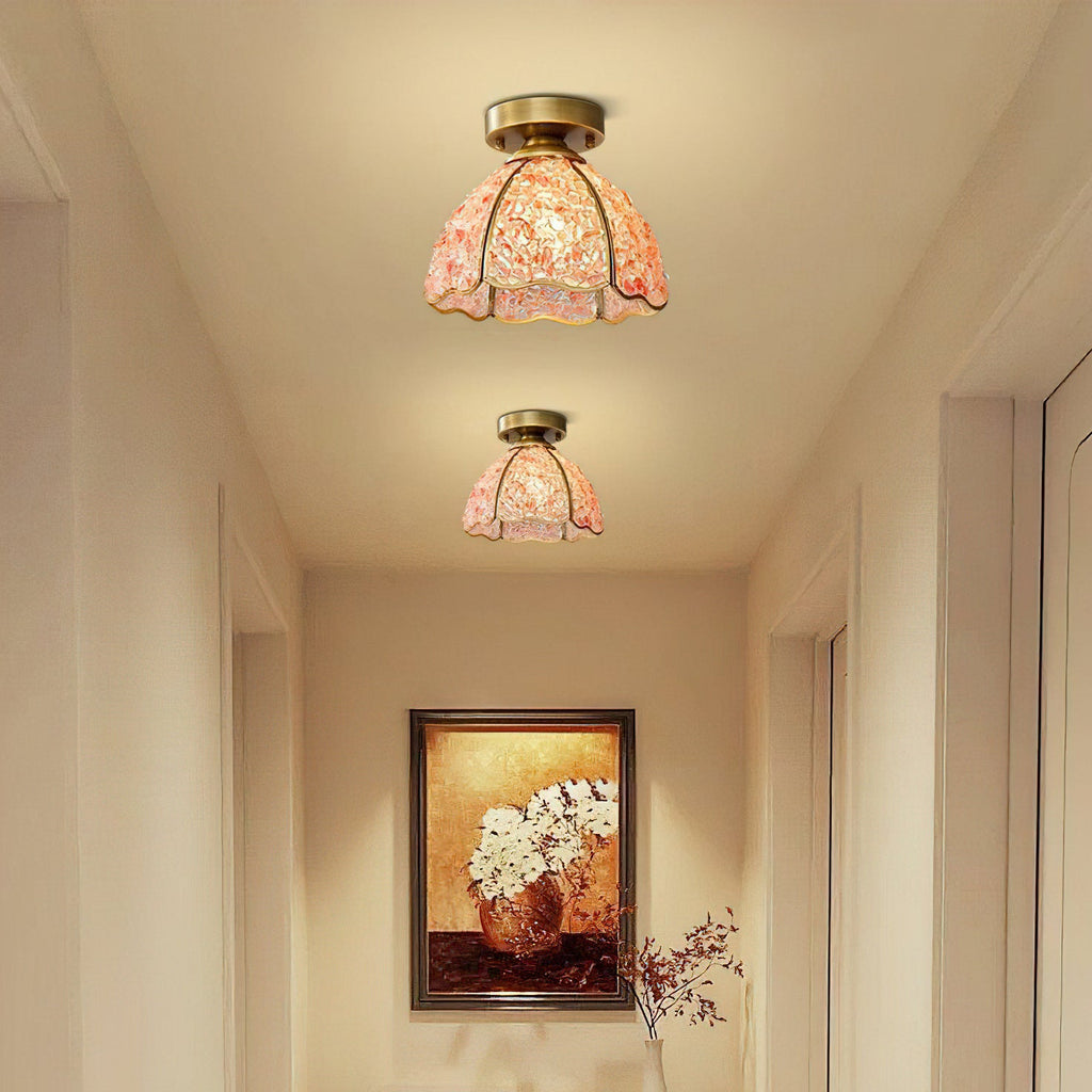 Lit pink glass ceiling lights above a narrow hallway, this Clérachic pair casting a warm peach glow on cream walls.