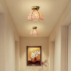 Lit pink glass ceiling lights above a narrow hallway, this Clérachic pair casting a warm peach glow on cream walls.