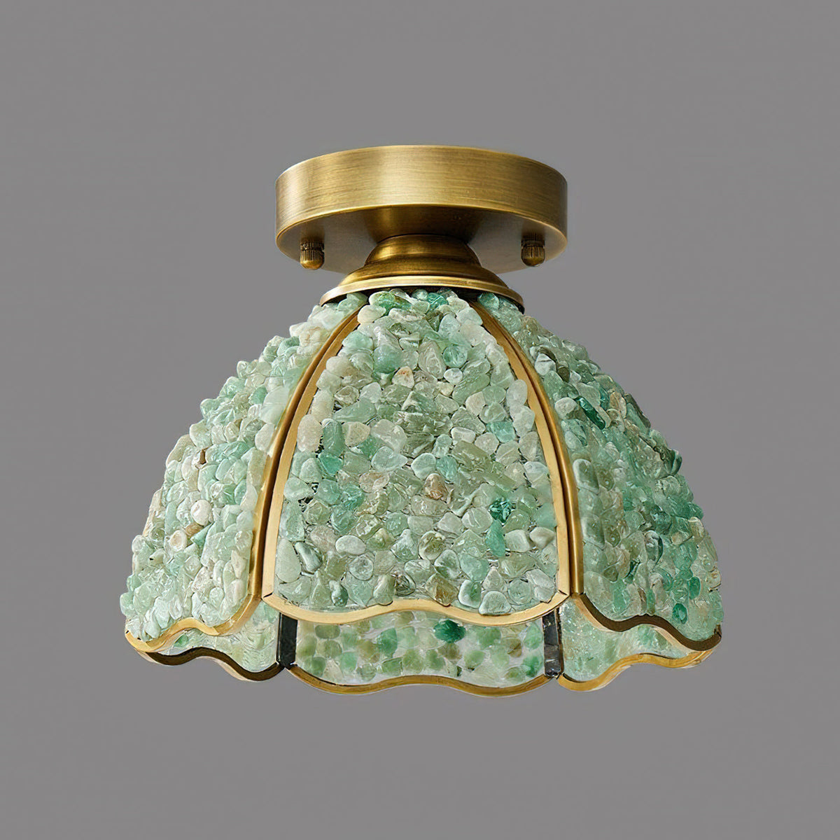 Side view of the green stone-chip shade, brass ribs dividing the panels, on this Clérachic ceiling light in front of grey.