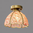 Lit pink version of this Clérachic ceiling light, its peach glass chips glowing warmly inside the brass-ribbed dome, on grey.