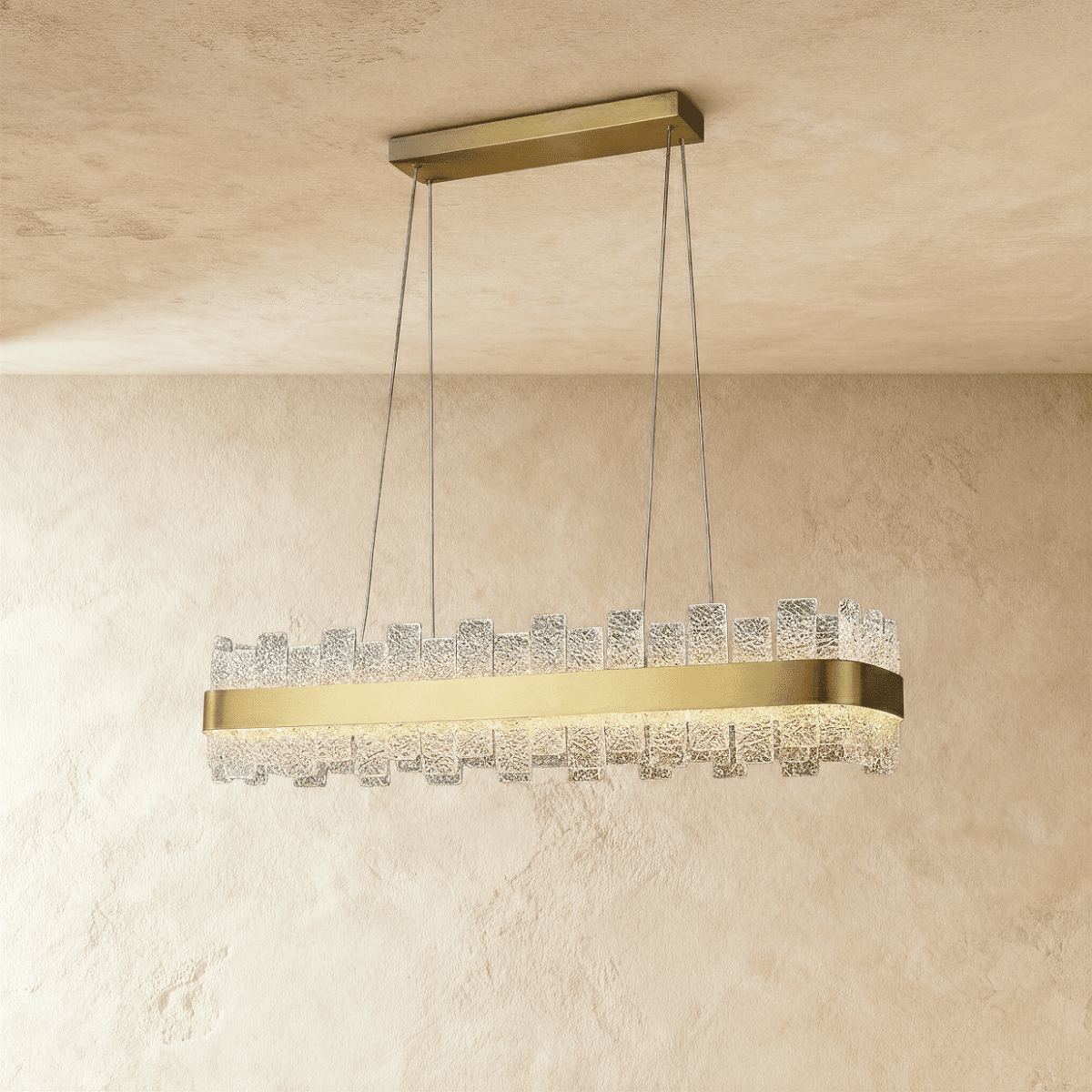 Clérachic linear chandelier with a brushed brass band and staggered textured glass panes, hanging on four cables from a bar canopy.