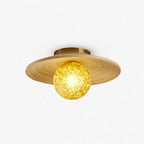 Yellow textured glass globe under a wide bamboo disc and brass canopy on this Clérachic ceiling light, on a plain white backdrop.