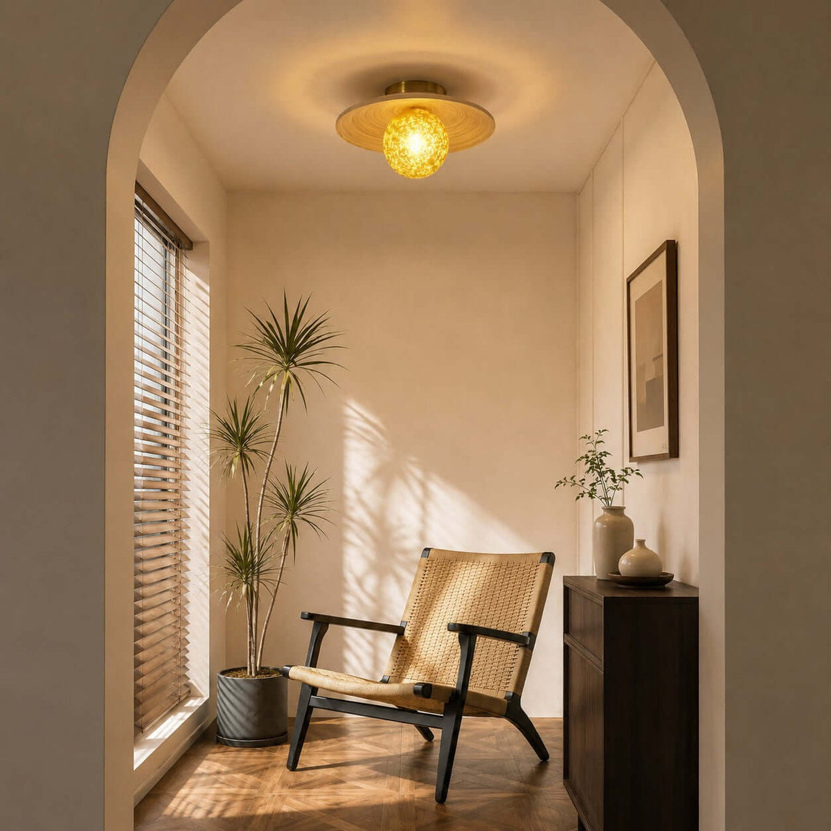 A Clérachic flush ceiling light with a yellow glass globe glows in an arched nook with a woven lounge chair and a tall plant.