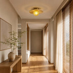 A yellow-globe Clérachic flush light with a bamboo disc hangs in a long hallway lined with wooden blinds and sheer curtains.