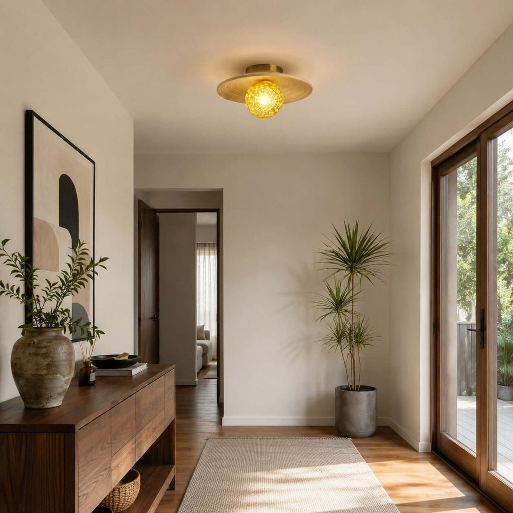 This Clérachic ceiling light with a glowing yellow globe sits above an entry area with a walnut console and a glass door.
