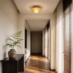 Lit from within, this Clérachic ceiling light with a bamboo disc hangs in a hallway with a dark console and herringbone floor.