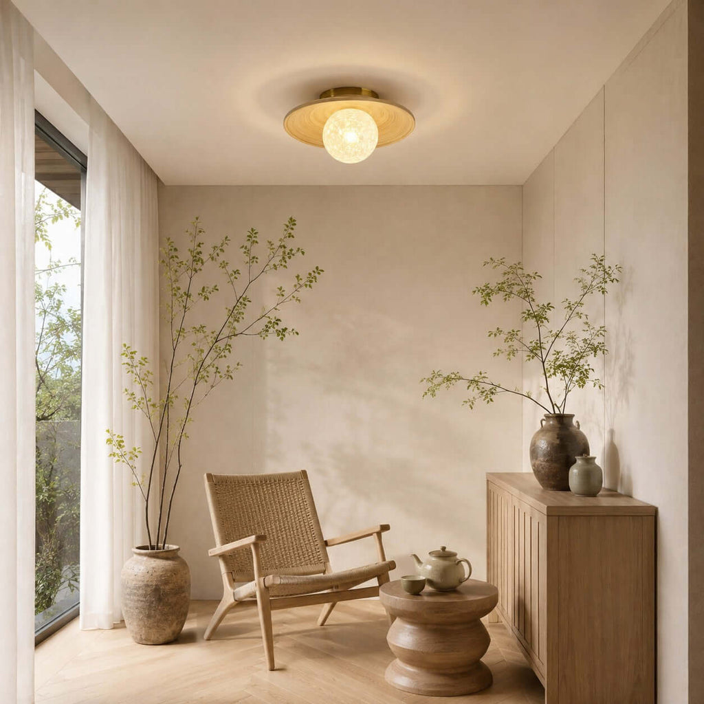 A white-globe Clérachic flush light with a bamboo disc hangs in a calm corner with a woven chair and a low wooden side table.
