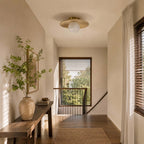 A Clérachic flush light with a pale globe and bamboo disc lights a landing with a wooden bench, a stone vase and a window.
