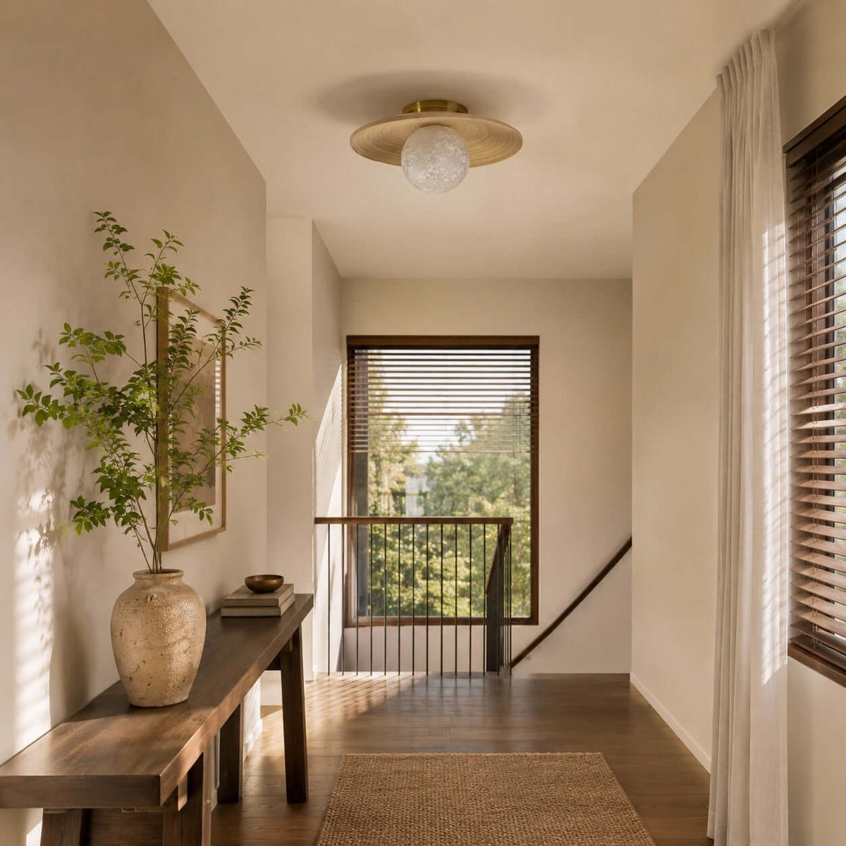 A Clérachic flush light with a pale globe and bamboo disc lights a landing with a wooden bench, a stone vase and a window.