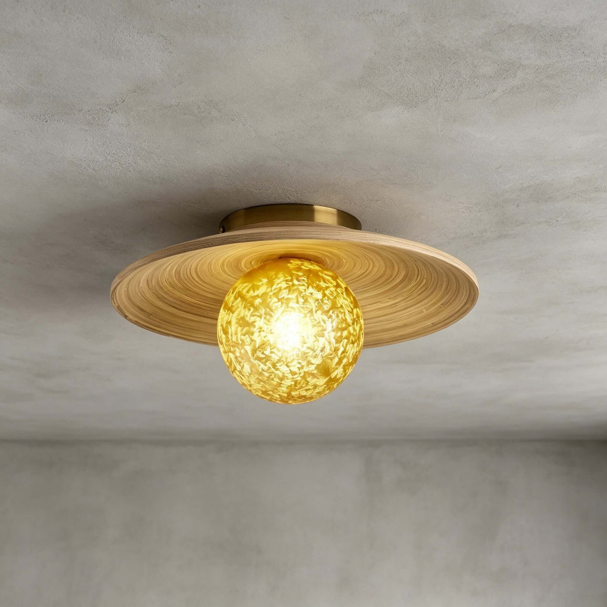 Close view of the spiral-grained bamboo disc and yellow ice-textured glass globe on this Clérachic ceiling light, on grey.