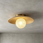 The white ice-textured glass globe and bamboo disc of this Clérachic ceiling light, with a brass canopy, on a grey wall.
