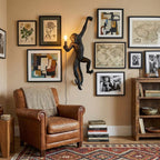 A black monkey wall light from Clérachic hangs among framed prints and maps, with a leather armchair and shelves below.