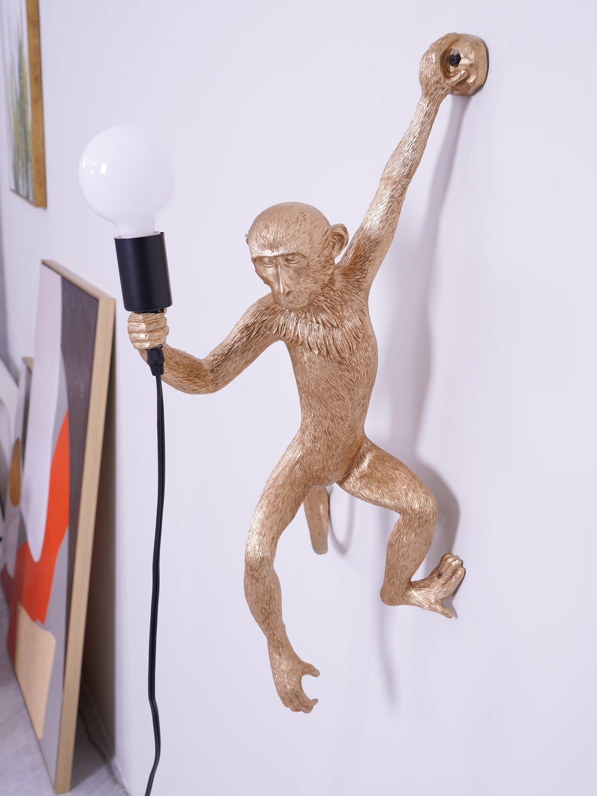 Detail of the gold resin monkey on this Clérachic wall light, its textured fur and long limbs shown against a lilac-white wall.