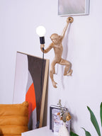 A gold monkey wall light from Clérachic reaches up to the wall with a bulb in hand, framed art and a cream vase below.
