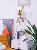Hanging high above a white cabinet, this gold Clérachic monkey light holds a bulb, with an orange chair and leafy plant nearby.