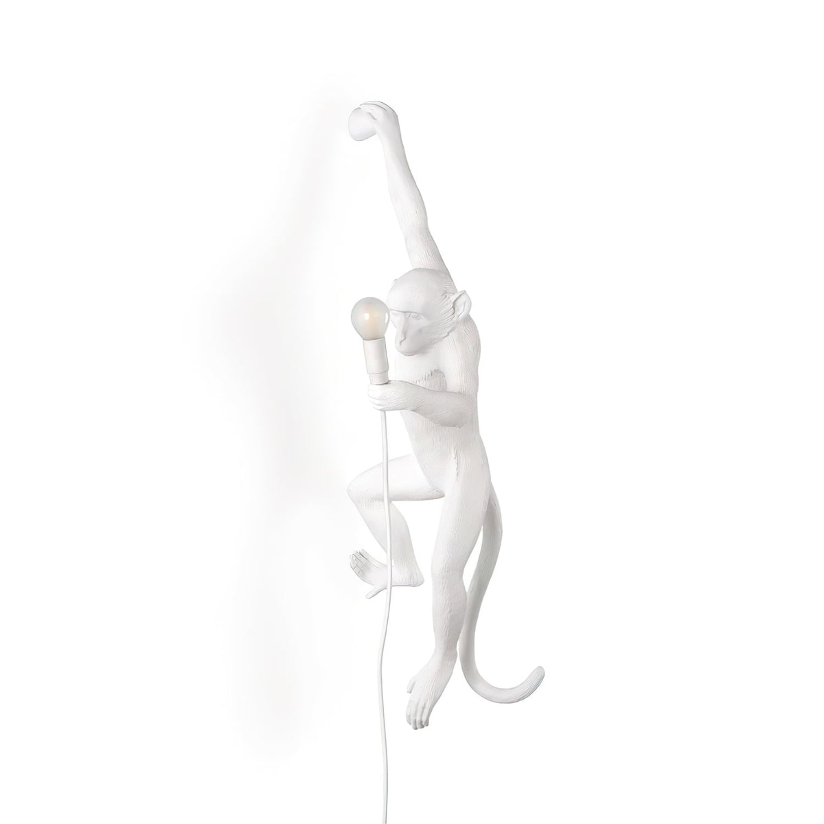 A white resin monkey wall light from Clérachic hangs by one arm on a white background, its bulb held close to its body.