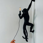 Black monkey wall light from Clérachic, close up on a pale wall, holding a filament bulb with its cord falling to a hand below.