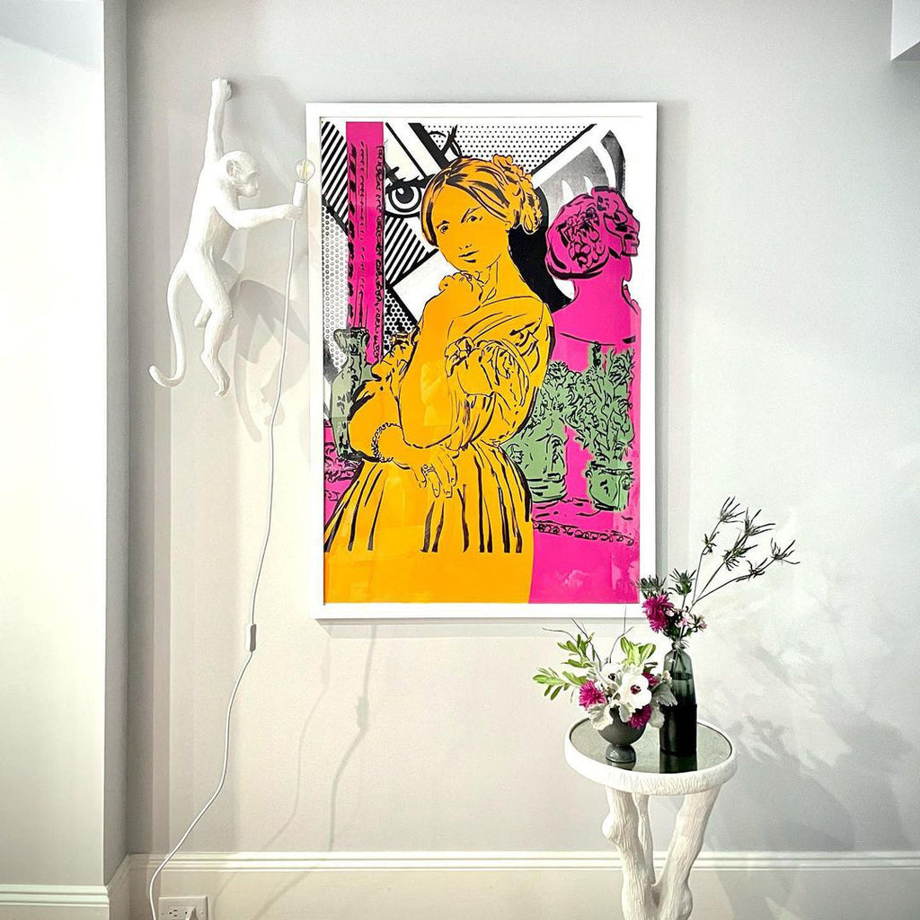 Far above a console table with a vase of flowers, a white Clérachic monkey wall light hangs beside a bold pink-and-yellow print.